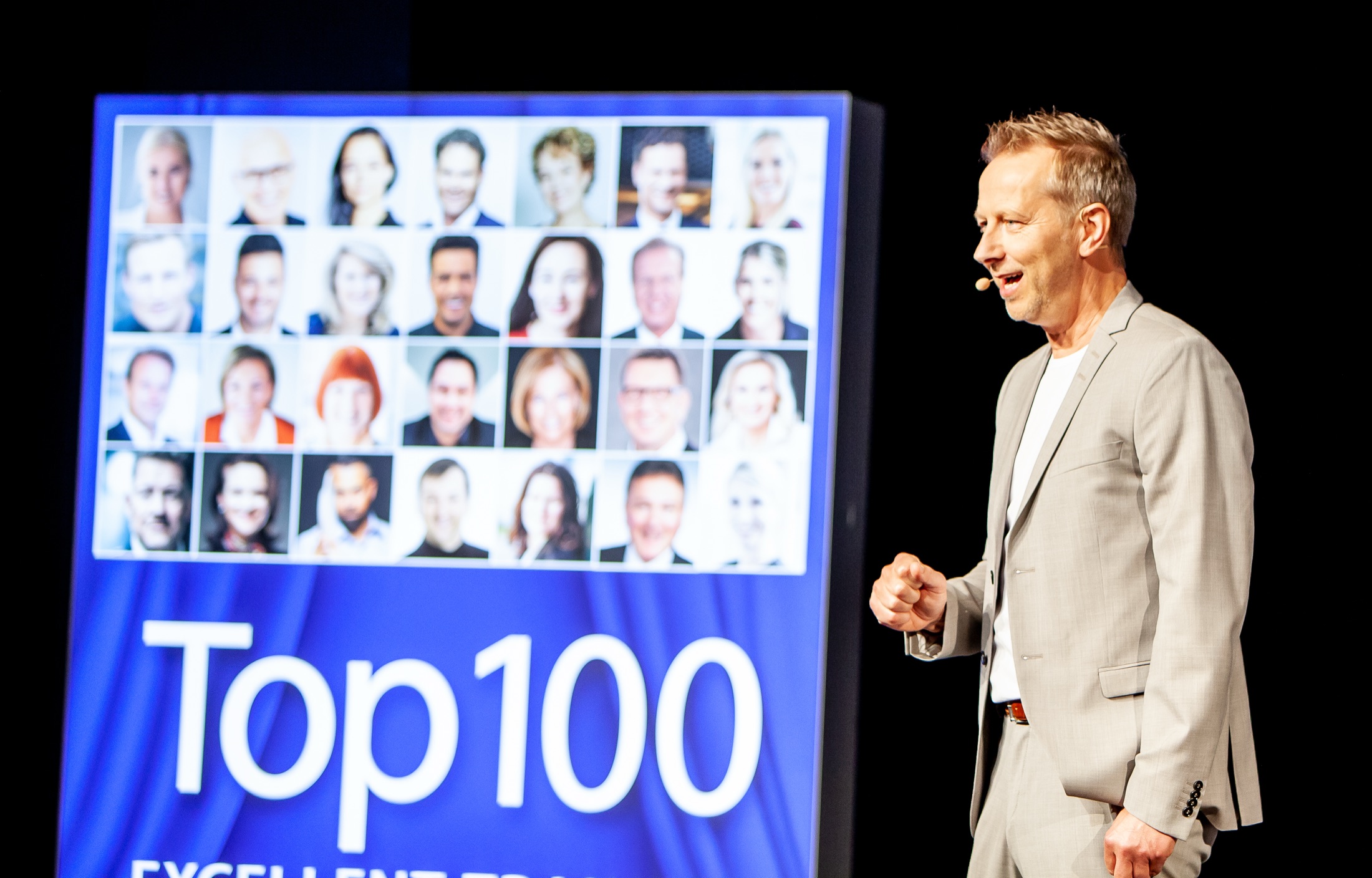 Rainer Stolte spricht auf einer großen Bühne vor einer Leinwand mit der Aufschrift Top 100